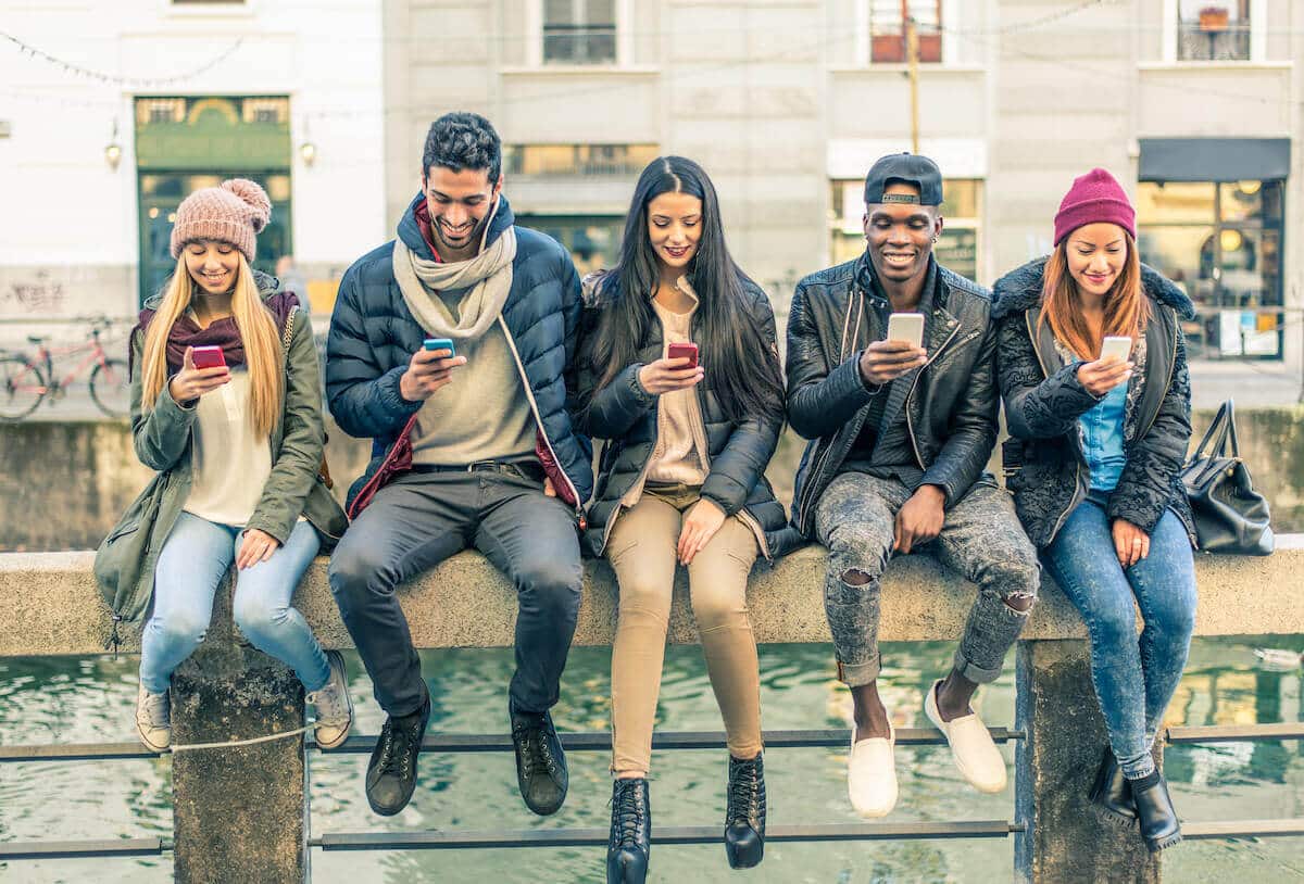 Five young adults sitting on a ledge looking at their smartphones